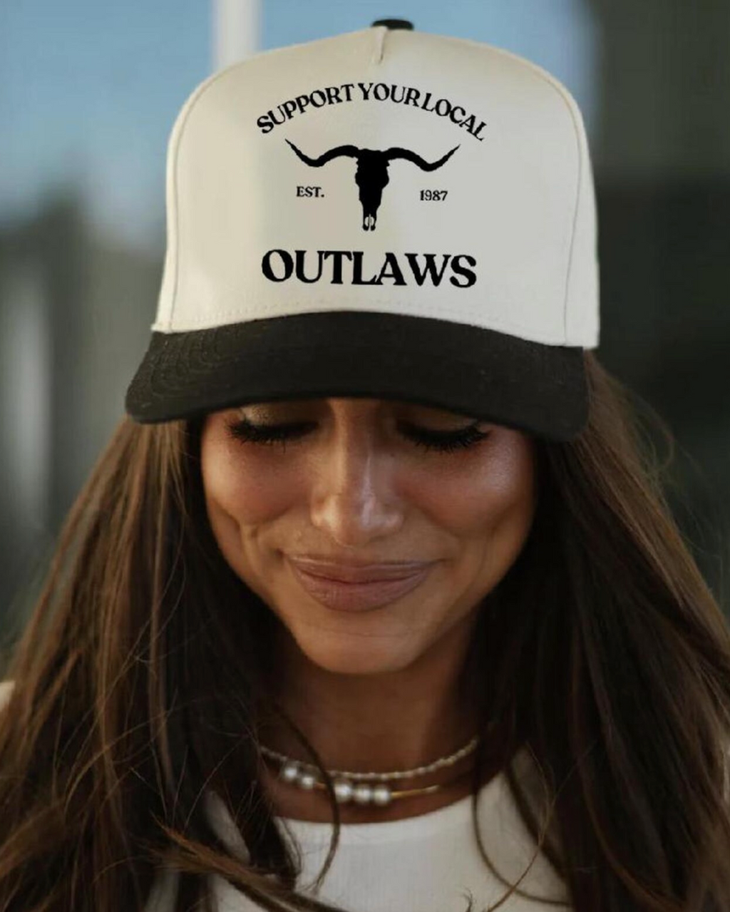 Woman wearing a cap with 'Support Your Local Outlaws' text and logo.