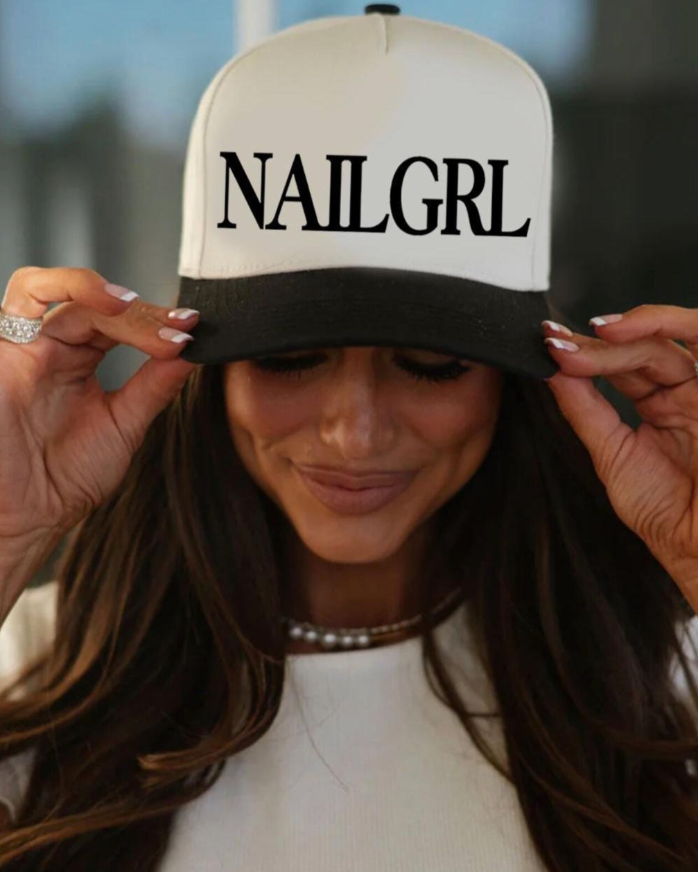 Person wearing a cap with 'NAILGRL' text, with blurred background