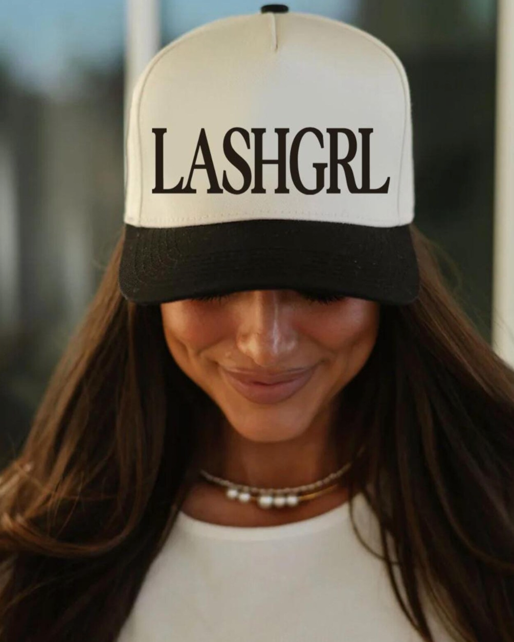Person wearing a cap with 'LASHGRL' text in an outdoor setting