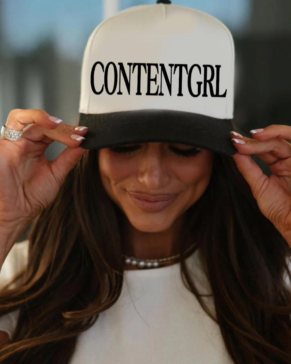 Person wearing a cap with 'CONTENTGIRL' text, with a blurred background