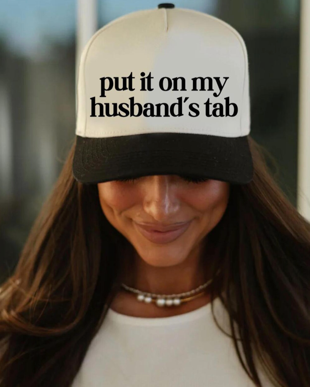 Woman wearing a cap with 'put it on my husband's tab' text