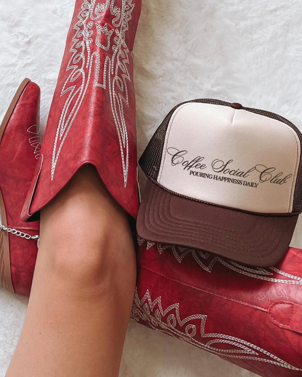 Red cowboy boots with white embroidery and a 'Coffee Social Club' cap on a light background