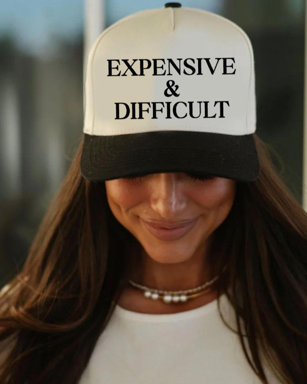 Person wearing a cap with 'EXPENSIVE & DIFFICULT' text