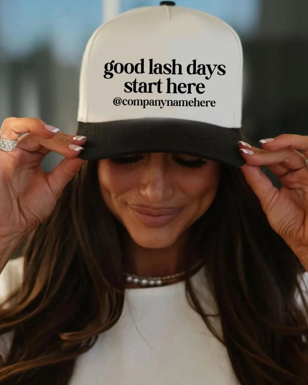 Person wearing a cap with 'good lash days start here' text, blurred background