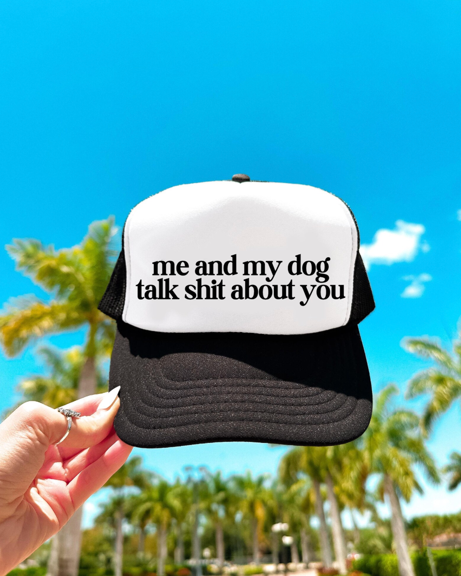 Black and white cap with text held against a blue sky and palm trees background