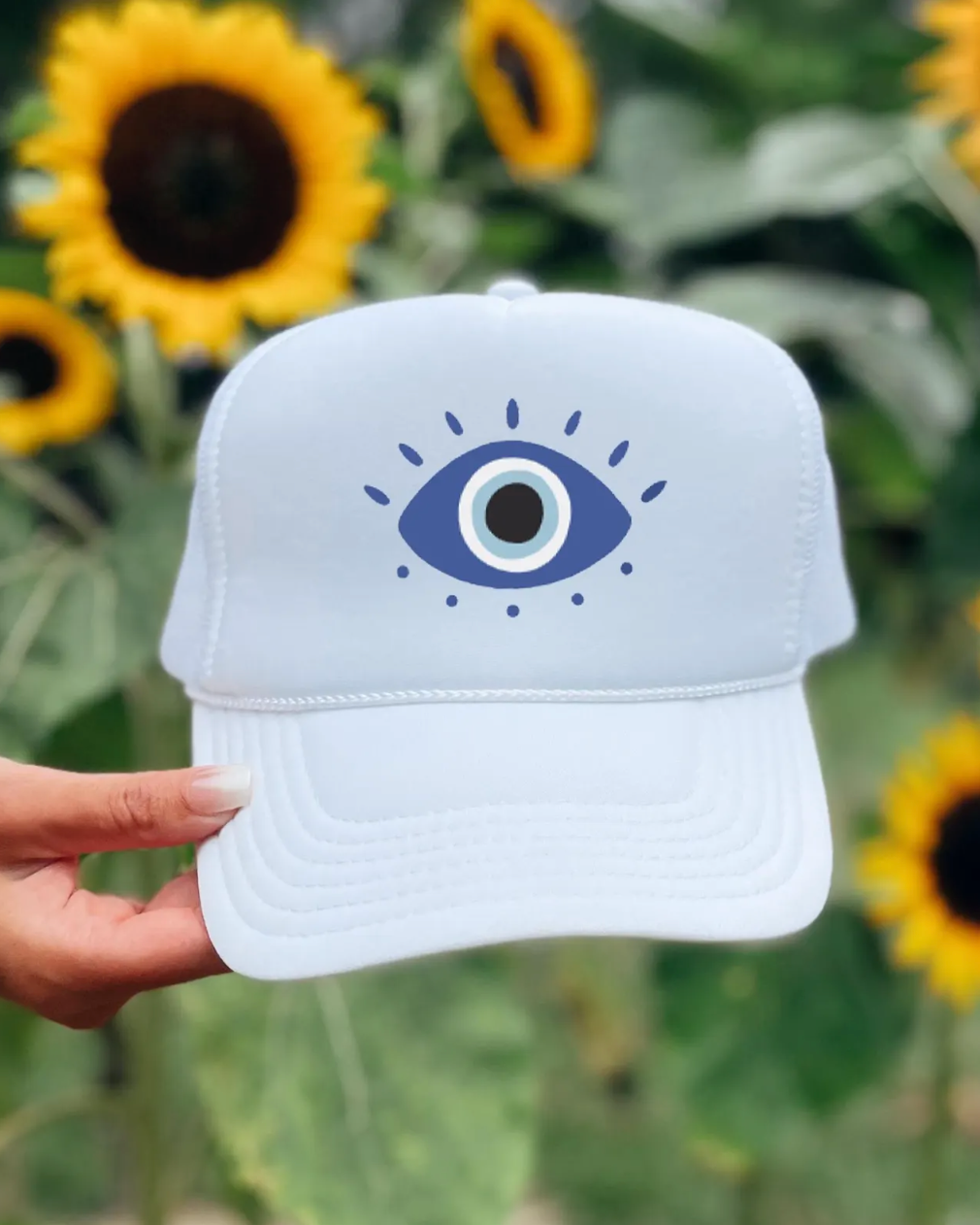 White cap with eye design held in front of sunflowers