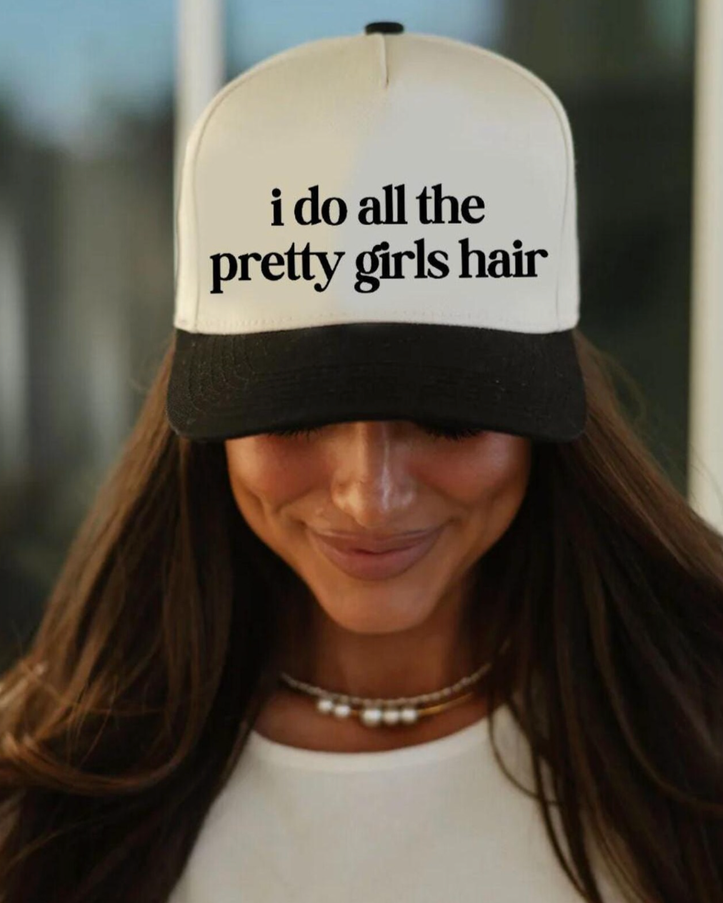 Person wearing a cap with 'i do all the pretty girls hair' text