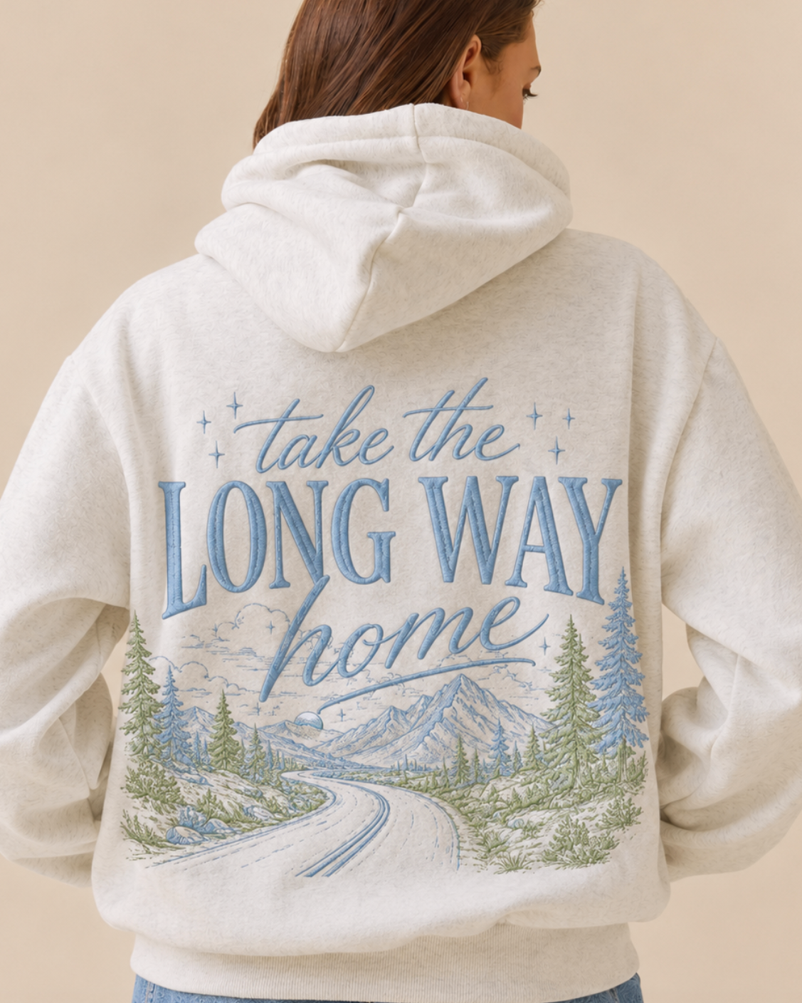Person wearing a hoodie with 'take the long way home' text and nature design on the back.