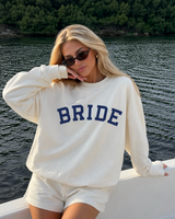 Woman wearing a 'BRIDE' sweatshirt by a body of water.