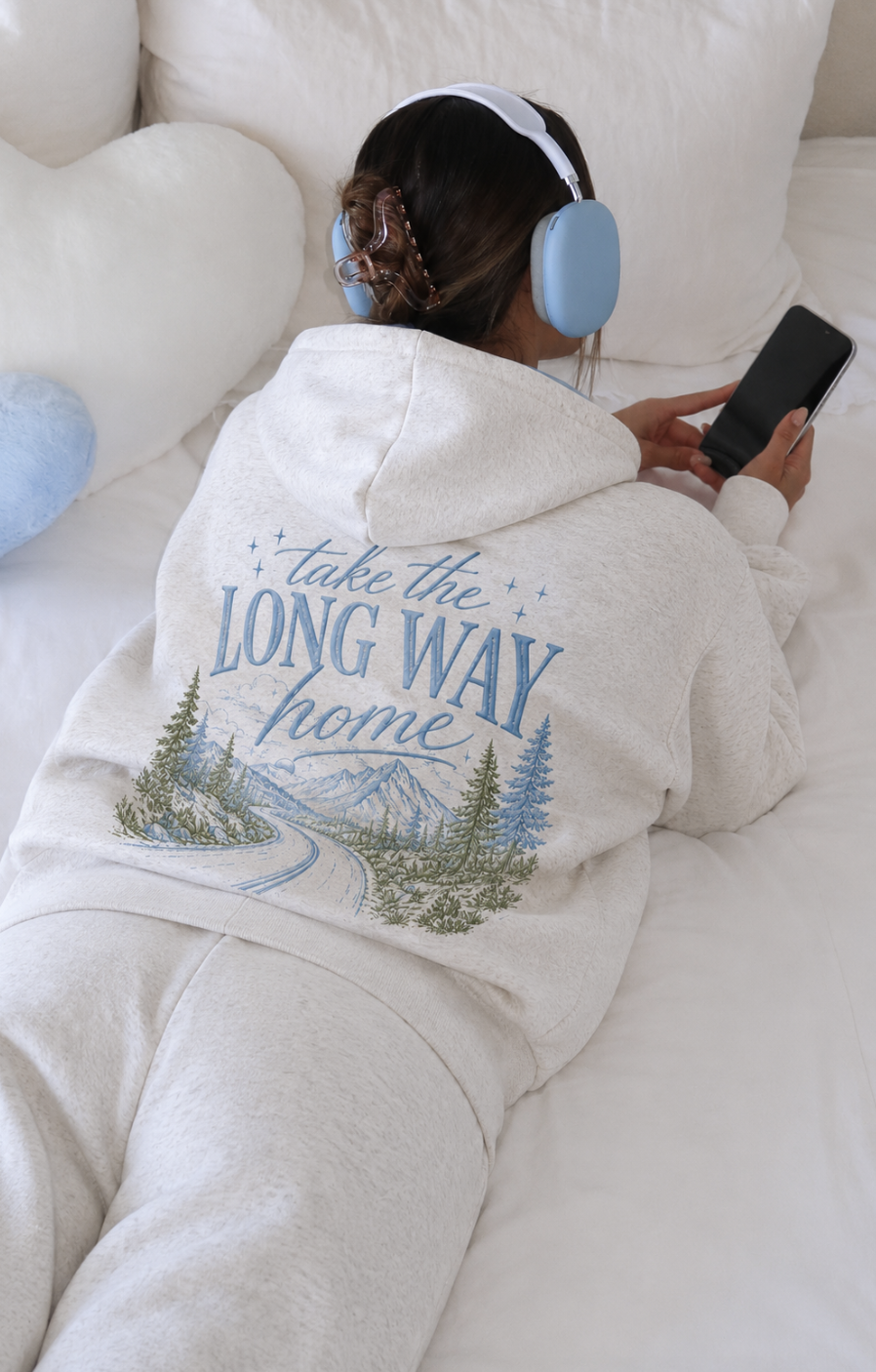 Person wearing a hoodie with a scenic design and text, sitting on a couch.