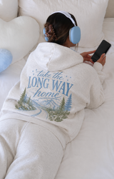 Person wearing a hoodie with a scenic design and text, sitting on a couch.