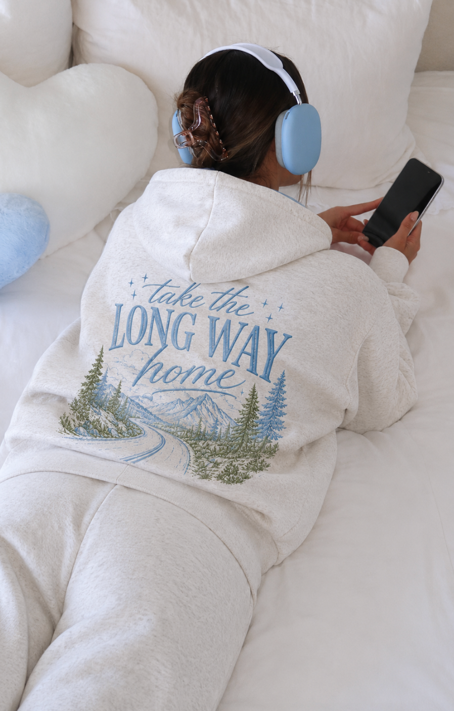 Person wearing a hoodie with a scenic design and text, sitting on a couch.