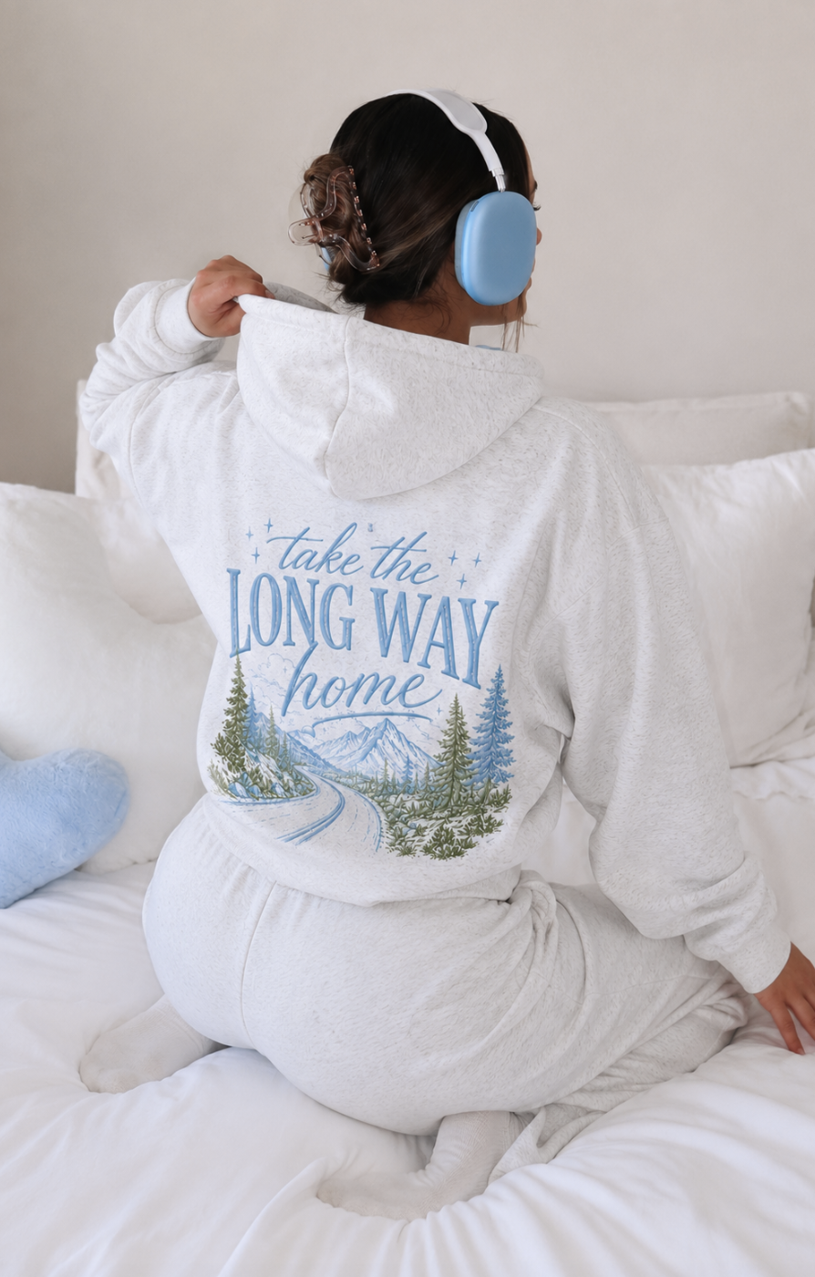 Person wearing a white hoodie with a scenic design and text, sitting on a couch.