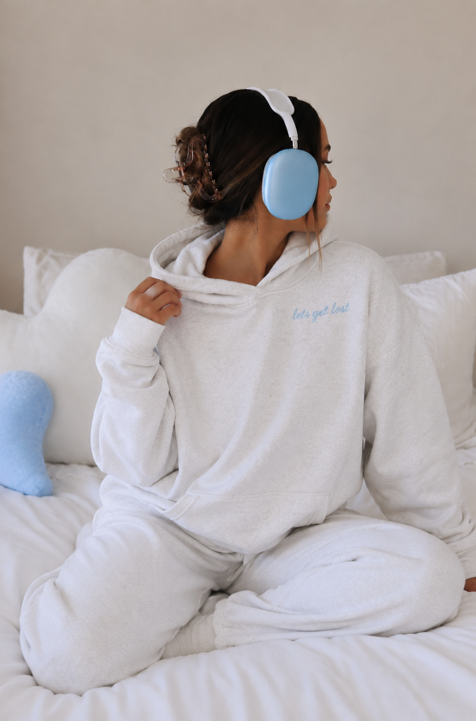 Person wearing a white hoodie and blue earbuds sitting on a bed.