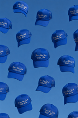 Multiple blue baseball caps with white embroidered text reading 'Love New York With Love' are arranged in a repeating pattern against a solid blue background.