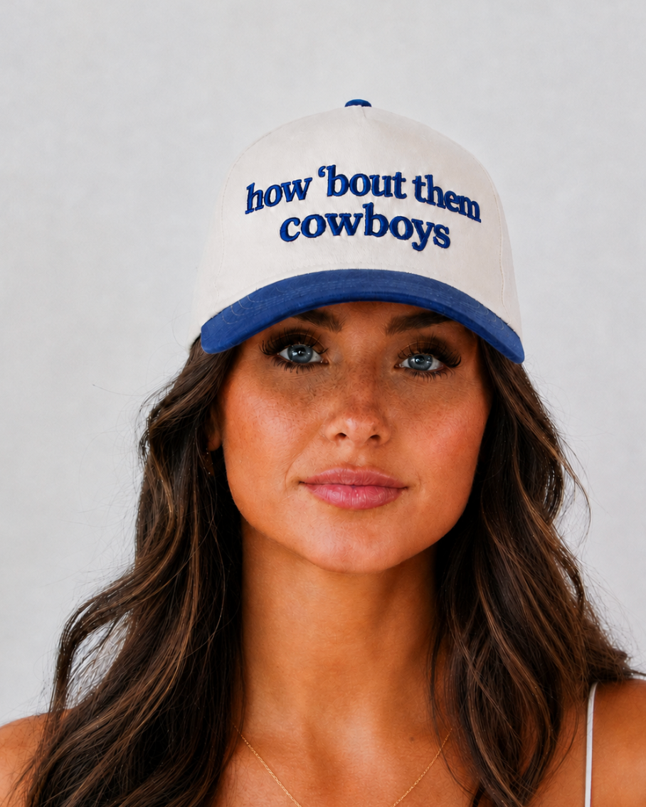 A woman wearing a white and blue baseball cap with the embroidered text 'how 'bout them cowboys' in blue on the front, photographed against a light gray background.