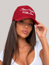 A woman wearing a red trucker-style baseball cap with white embroidered text reading 'From Houston With Love' on a light gray studio background.