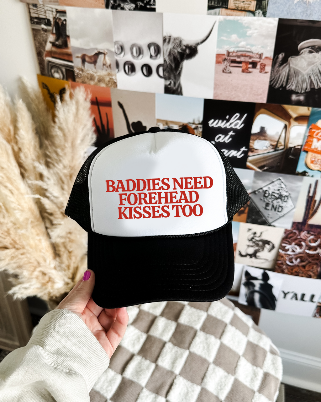 Trucker hat with 'Baddies Need Forehead Kisses Too' text held in front of a collage of photos.