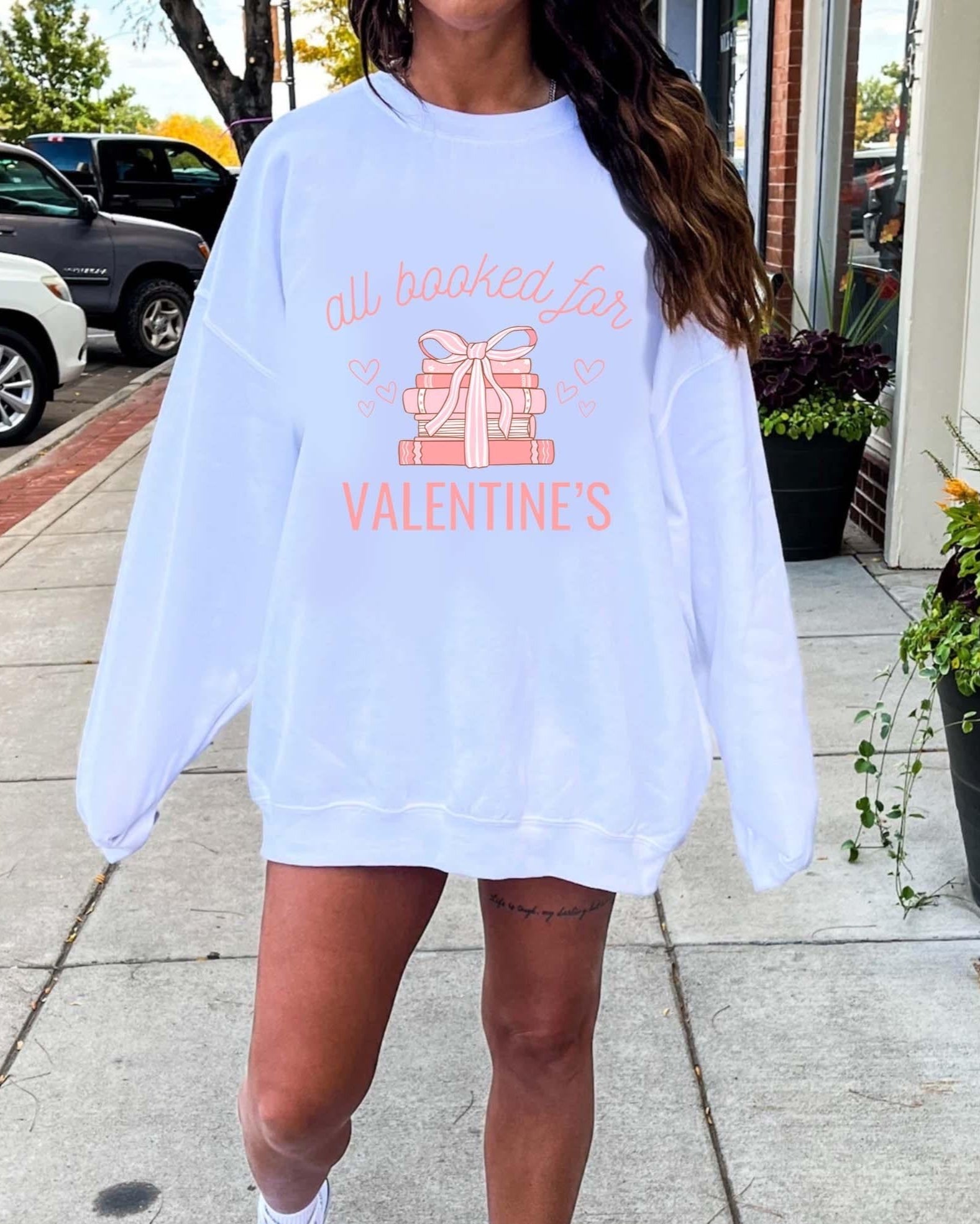 A woman wearing a white sweatshirt with the text 'All booked for Valentine's' in a crewneck style.