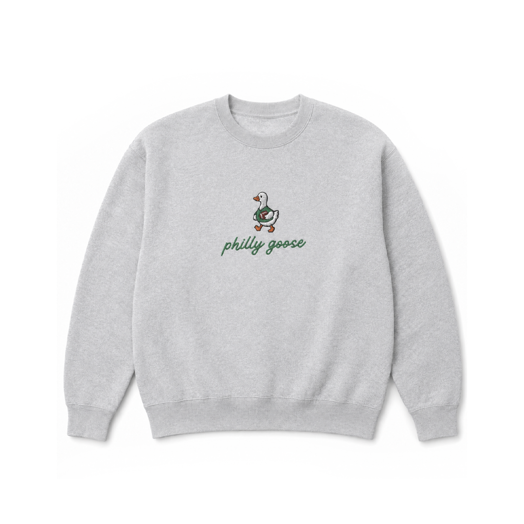 A light heather gray crewneck sweatshirt featuring a small embroidered Philadelphia goose graphic and the text 'philly goose' in green script on the chest, displayed against a solid white background.