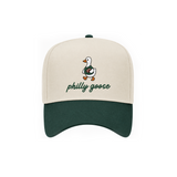 A baseball cap with an off-white crown and a dark green visor, featuring an embroidered walking duck wearing a green sweater with 'philly goose' written below in green script.