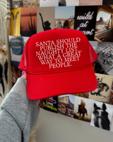 Red cap with humorous text held in front of a wall with various posters and decorations.